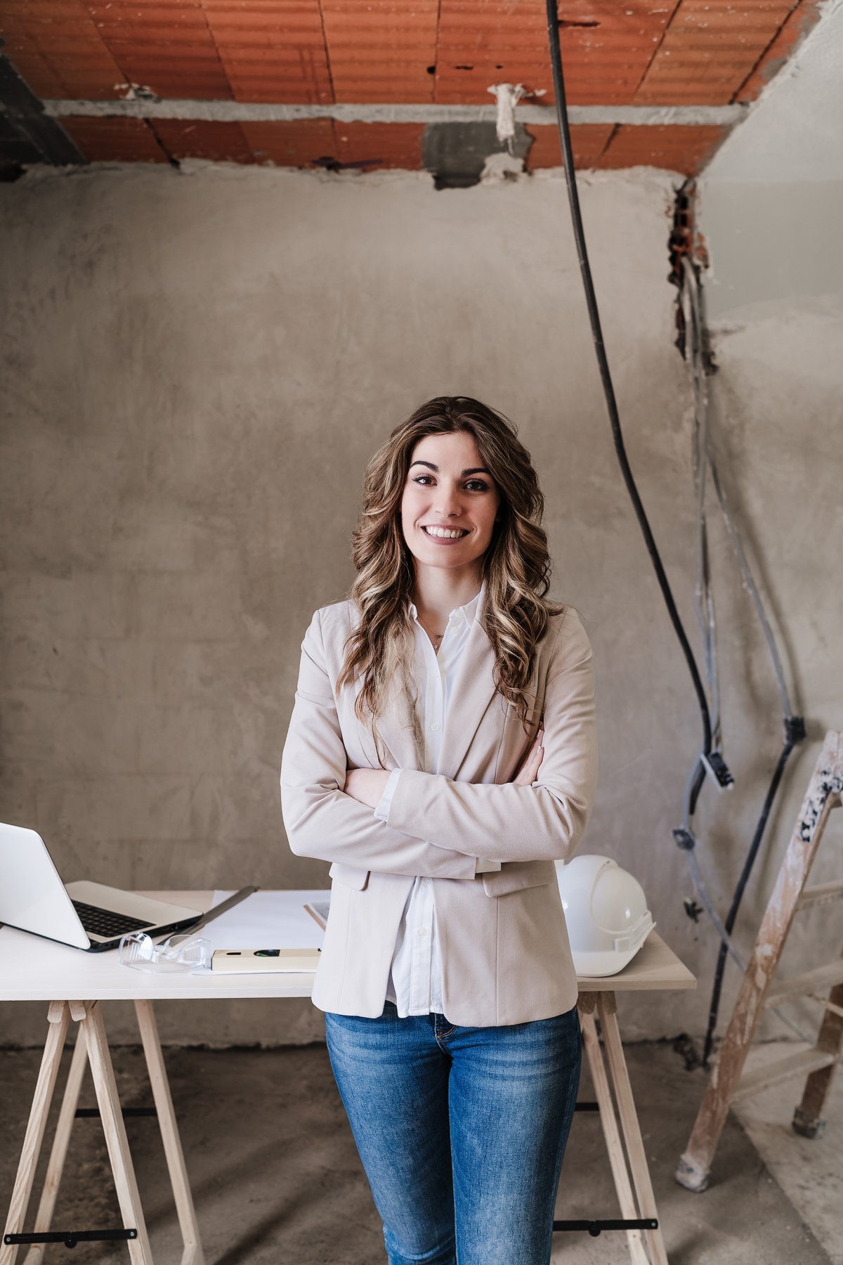 Diseñadora en un espacio en obra, de pie con los brazos cruzados y una expresión de confianza.