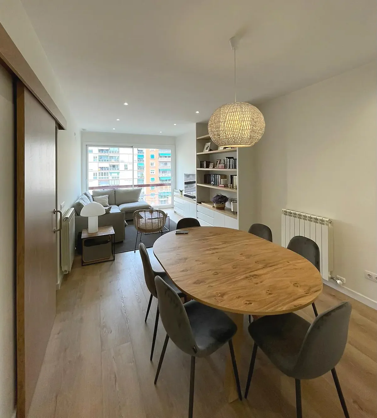 Salón comedor moderno con mesa de madera ovalada, sillas grises y lámpara colgante.