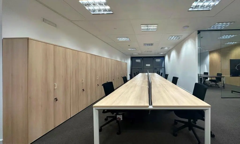 Oficina moderna con mesas de trabajo compartidas y armarios de almacenamiento en madera clara.