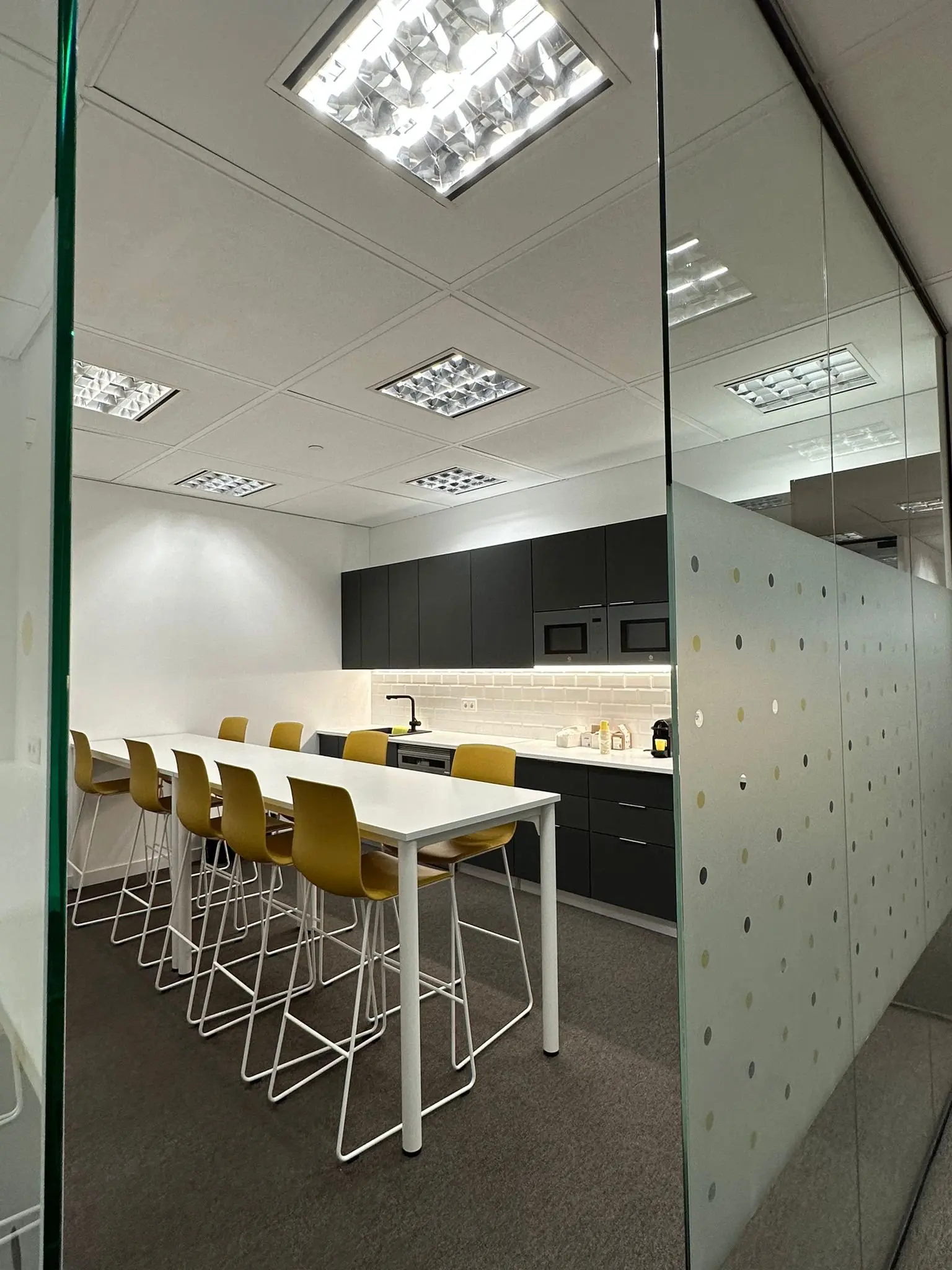 Cocina office moderna en oficina, con barra alta y sillas amarillas.