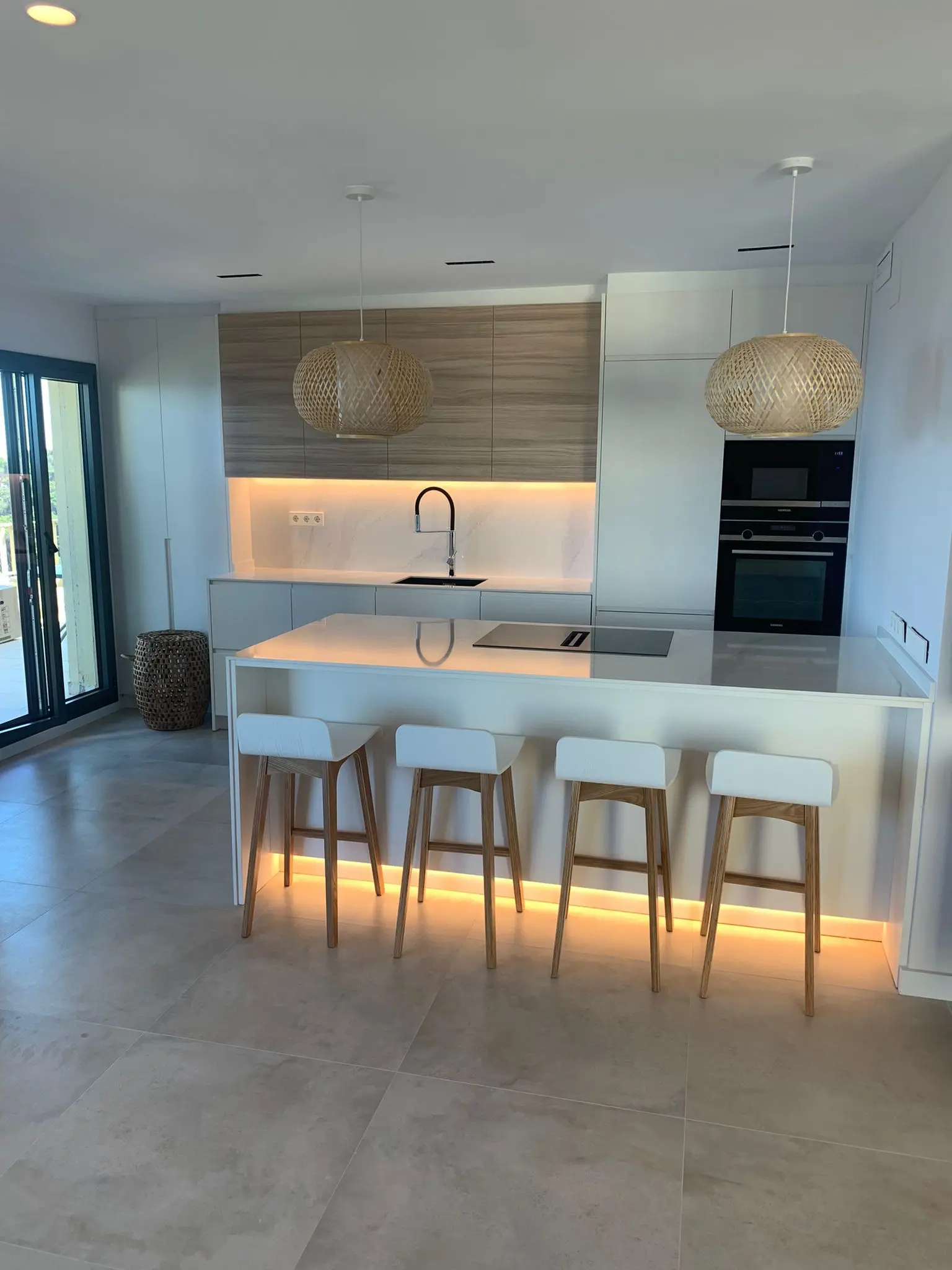 Cocina moderna con isla, iluminación LED y taburetes de madera y blanco.